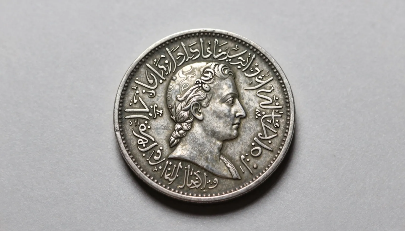 Mughal silver rupee coin with Persian calligraphy inscriptions photographed on neutral studio surface for numismatic identification
