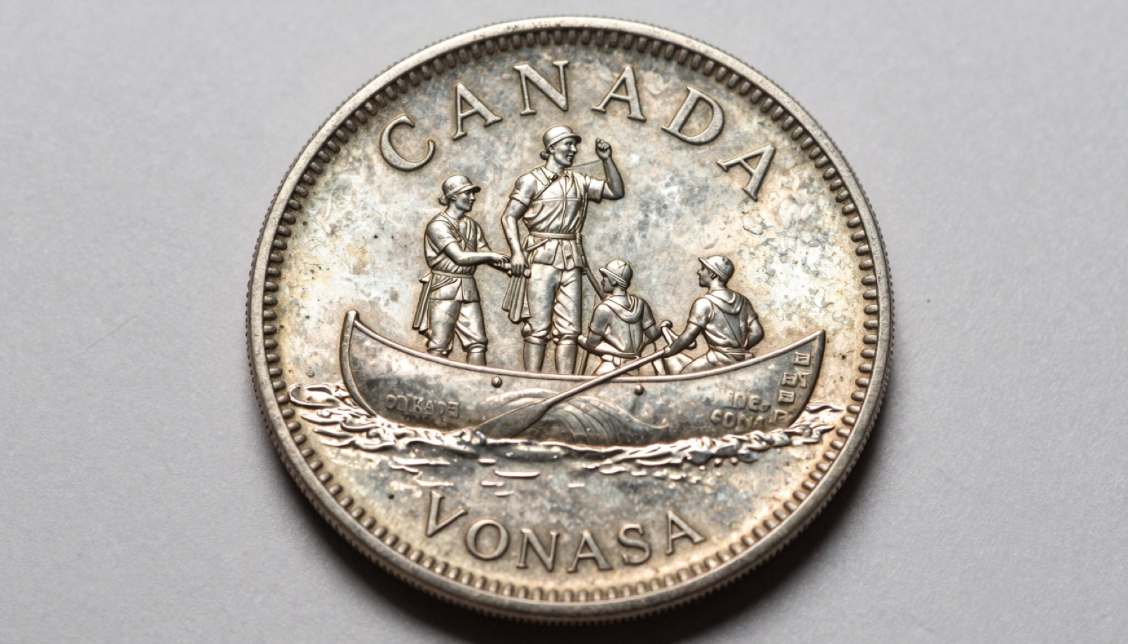 Genuine 1935 to 1967 Canadian voyageur silver dollar on neutral studio surface showing reverse canoe and paddlers design detail